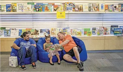  ??  ?? ABOVE: Jim Reynolds reads to his granddaugh­ter Alina Perez, 7, as her father, Angel, listens. The family stopped by Oklahoma City Public School’s Reading Room during a recent visit to Penn Square Mall.