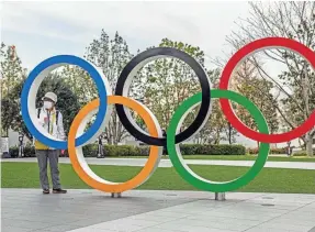  ?? CARL COURT/GETTY IMAGES ?? A woman wearing a face mask poses for a photograph next to the Olympic rings in Tokyo, host of the next Summer Olympics.