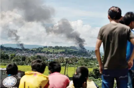  ??  ?? People watch as smoke billows from houses after airstrikes hit militant positions in Marawi on the southern Philippine island of Mindanao on Saturday. (AFP)