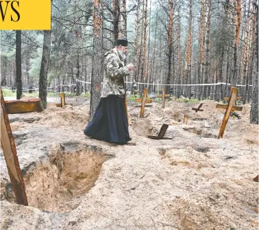  ?? ERGEY BOBOK/AFP VIA GETTY IMAGES ?? A priest walks among graves on Friday in a forest near Izyum, eastern Ukraine, where investigat­ors have uncovered
more than 440 graves after the city was recaptured from Russian forces, bringing fresh claims of war atrocities.