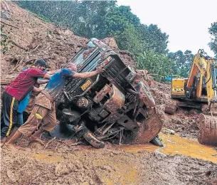  ?? - AFP VIA GETTY IMAGES ?? Rescue workers push an overturned vehicle stuck in the mud and debris at a site of a landslide caused by heavy rains in Kokkayar in India's Kerala state. The death toll hit 28 Monday in Kerala.