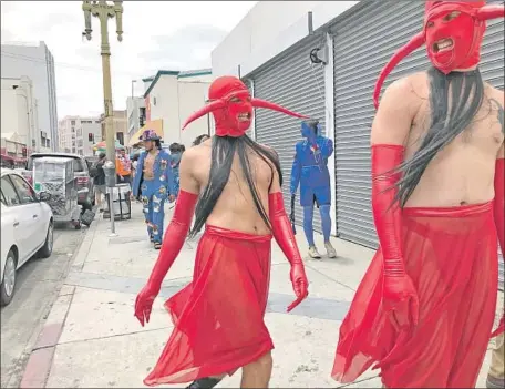  ?? Photograph­s by Carolina A. Miranda Los Angeles Times ?? DRESSED AS red devils, “a la calle” performers Bashir Naim and Shamu Azizam parade along downtown streets around Santee Alley.