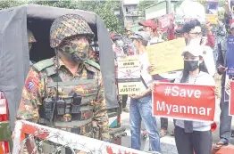  ?? — AFP photo ?? A soldier stands guard next to protesters holding signs during a demonstrat­ion against the military coup outside the Central Bank of Myanmar in Yangon.