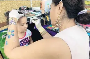  ?? PHOTOS BY MARCO SANTANA/STAFF ?? Zaida Goitia paints Isabela Salaz’s face during the Earth Day celebratio­n at Lake Eola on Saturday.