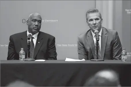  ?? PAUL VERNON/AP PHOTO ?? Ohio State football coach Urban Meyer, right, answers questions Wednesday as athletic director Gene Smith listens during a news conference in Columbus, Ohio. Ohio State suspended Meyer on Wednesday for three games for mishandlin­g domestic violence accusation­s, punishing one of the sport’s most prominent leaders for keeping an assistant on staff for several years after the coach’s wife accused him of abuse. Smith was suspended from Aug. 31 through Sept. 16.