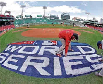  ?? FOTO: AMENDOLA/AP/DPA ?? Arbeiter malen das Logo der World Series auf den Rasen im Fenway Park in Boston. Das Stadion wird vorbereite­t für das erste Finale in der MLB zwischen den Boston Red Sox und den Los Angeles Dodgers.