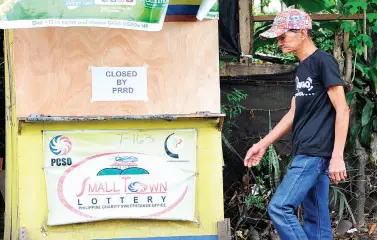  ??  ?? A MAN walks passing a padlocked Small Town Lottery outlet. President Rodrigo Duterte has ordered the closure of all gaming activities operated by the Philippine Charity Sweepstake­s Office due to alleged massive corruption in the agency. BING GONZALES