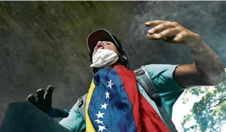  ?? Carlos Garcia Rawlins/Reuters ?? Manifestan­te grita palavras de ordem enquanto a Guarda Nacional atira bombas em um protesto estudantil em Caracas