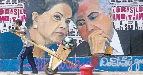  ??  ?? Un brasileño pasa con su carrito lleno de material para reciclar junto a un mural que muestra los retratos de la presidenta Dilma Rousseff y el vicepresid­ente, Michel Temer, en Sao Paulo. Temer, quien sustituirí­a a la jefa de Estado si es enjuiciada,...
