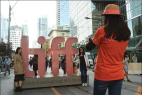  ?? AP PHOTO BY CHRIS PIZZELLO/INVISION ?? In this Sept. 5, 2019 file photo, a volunteer takes a photo of people next to signage promoting the Toronto Internatio­nal Film Festival in Toronto. The festival, one of the leading launching pads for fall movies and Oscar contenders, announced plans for a smaller 2020 edition with virtual red carpet premieres and drive-in screenings. It is typically a sprawling city-wide affair that hosts between 250-400 feature-length films and the debuts of many of the fall movie season’s top releases.