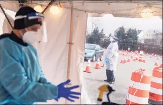  ?? David Goldman / Associated Press ?? In this photo taken Wednesday, health care workers prepare to test motorists for COVID-19 at a testing site outside McCoy Stadium in Pawtucket, R.I.