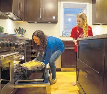  ?? E. JASON WAMBSGANS/CHICAGO TRIBUNE ?? Roscoe Village resident Marci Sieracki pulls a lasagna out of the oven while her daughter Charlotte watches on Nov. 25, 2020. Sieracki bakes and delivers lasagna for free to health care workers and other people affected by COVID-19 as part of a national Lasagna Love movement.