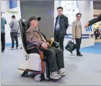  ?? XINHUA ?? An employee helps a visitor to experience a multi-functional wheelchair designed for elderly healthcare at a fair in Shanghai.