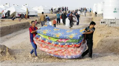  ??  ?? HASSAN SHAM, Iraq: Displaced Iraqi men, who fled from Mosul, carry mattresses at a camp for internally displaced people east of Mosul yesterday. — AP