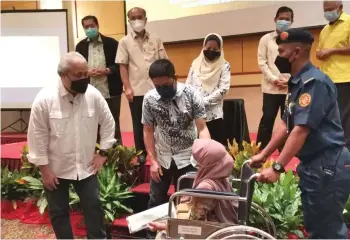  ??  ?? Ripin (second left) presents a land title to a wheelchair-bound landowner from Kampung Beraya, witnessed by Awang Tengah (left), Rosey (back row, centre) and others.