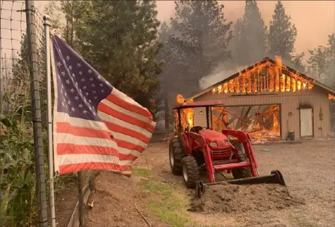  ?? Eugene Garcia/Associated Press ?? A red tractor is left behind as a home burns Friday as part of the Dixie Fire outside of Taylorsvil­le in Plumas County, Calif.