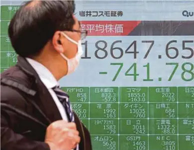  ?? AFP PIC ?? A man wearing a face mask walking past a quotation board displaying share prices of the Tokyo Stock Exchange in Tokyo yesterday.