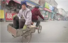  ?? — AFP ?? BEIJING: An elderly man sits on the back of a tricycle ridden by an elderly woman in the Heiqiaocun migrant village in Beijing.