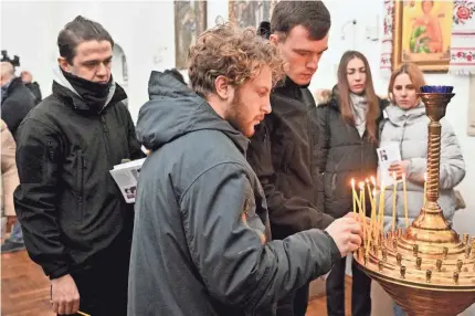  ?? SERGEI SUPINSKY/AFP VIA GETTY IMAGES ?? Friends and colleagues of Andrew Bagshaw place candles during a memorial service in Kyiv Sunday. Bagshaw and fellow volunteer Chris Parry were killed while trying to evacuate people from a front-line town.