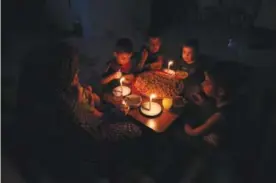  ?? — AFP ?? GAZA: A Palestinia­n family eats dinner by candleligh­t at their makeshift home in the Rafah refugee camp in the southern Gaza Strip during a power outage on Sunday.