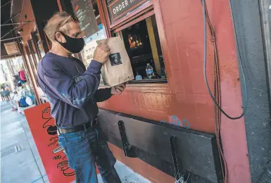  ?? Nick Otto / Special to The Chronicle ?? Lusiron Silvira, a driver for Postmates, picks up his delivery from Popsons Burgers in San Francisco.