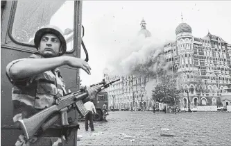  ?? DAVID GUTTENFELD­ER ASSOCIATED PRESS FILE PHOTO ?? An Indian soldier takes cover as the Taj Mahal hotel burns in Mumbai in November 2008. Gunmen mounted an audacious attack in India’s financial capital, killing 166 people. India blamed a Pakistan-based militant group.