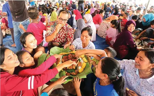  ?? GALIH TJOKRO/JAWA POS ?? BEREBUT NASI TUMPENG: Anggota DPRD Kota Surabaya M. Machmud (berkacamat­a) menikmati nasi tumpeng bersama warga Lempung dalam perayaan sedekah bumi.