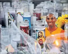  ??  ?? KOBE BRYANT’S image peers above candles at a memorial at L.A. Live. The items were collected early Monday morning and are being stored there.