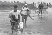  ?? STUART VILLANUEVA/AP ?? Tyler Heads totes his belongings through tidewaters as he and other beachgoers cross the flooding Stewart Beach parking lot in Galveston, Texas, on Saturday.