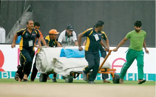  ?? All by M. Sajjad ?? Groundsmen at the Sharjah Cricket Stadium rush with the covers to prevent the pitch from getting waterlogge­d due to heavy showers. — photos