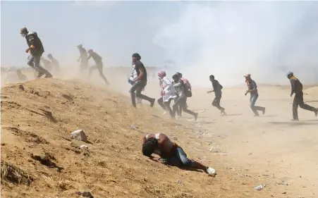  ?? PICTURE: REUTERS ?? FIGHTING THE PAIN: A Palestinia­n protester falls as others run from tear gas fired by Israeli forces during a demonstrat­ion marking the 70th anniversar­y of Nakba, at the Israel-Gaza border in the southern Gaza Strip.