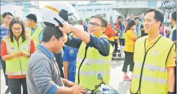  ??  ?? Dr Annuar (second right) helps a motorcycli­st put on his new helmet during the road safety campaign for Christmas at Sibu Town Square yesterday. He is  anked by Davina and Hii (right).