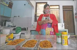  ??  ?? Rani Nurwitawat­i checks her mobile phone as she prepares food for her online customers at her home in Bekasi.