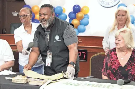  ?? PHOTOS BY MAYA WASHBURN/PALM BEACH POST ?? Mayor Roger Michaud laughs as he unravels a 75th-anniversar­y Lake Park T-shirt at the town’s 100th anniversar­y on Nov. 16. With him are Centennial Committee members Evelyn Harris Clark, left, and Patricia Leduc and Vice Mayor Kim Glas-Castro.