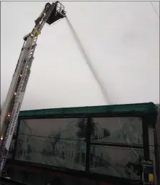  ??  ?? Fire fighters on a hydraulic lift dousing the fire on the roof.