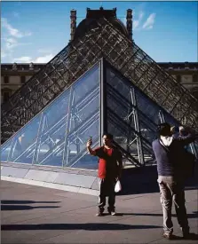  ?? Getty Images ?? Tourists take pictures near the pyramid at the Louvre Museum in Paris.