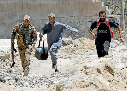  ??  ?? An Iraqi soldier and civilians run to avoid Islamic State snipers in the Shifa neighbourh­ood in western Mosul. The militants are using civilians as human shields, and have gunned down hundreds who have tried to flee the city in recent weeks.