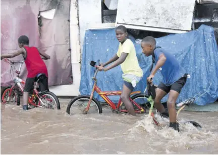  ?? (Photo: Karl Mclarty) ?? Boys wade through flood waters on Henley road in Waterhouse yesterday afternoon, where a little girl fell into the raging waters of the Sandy Gully after heavy downpour.