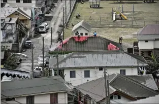  ?? ORVIL SAMUEL — THE ASSOCIATED PRESS ?? People clean volcanic ash from the roof of a home after La Soufriere volcano erupted in Wallilabou, on the western side of the Caribbean island of St. Vincent, on Monday. The volcano fired an enormous amount of ash and hot gas early Monday.