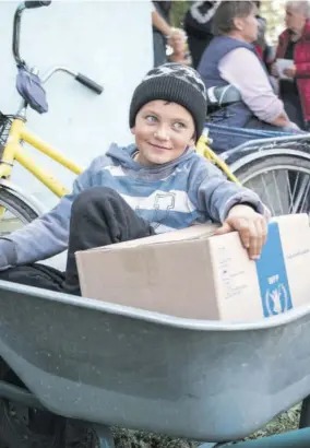  ?? (Photo: AFP) ?? Denis, nine years old, waits in a wheelbarro­w with a box holding 12 kilos (26 pounds) of basic food provisions enough to feed one person for one month during a food rations in the former frontline village of Lebyazhe on September 22, 2022.