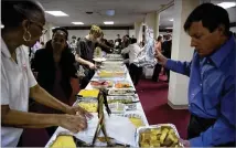  ??  ?? Jackie Davis, of First Baptist Church on New Street, (far left) and Needham Summerlin, of First Baptist Church of Christ on High Place, (far right) set out bread at First Baptist Church’s Thanksgivi­ng potluck as others from the two churches fix their...