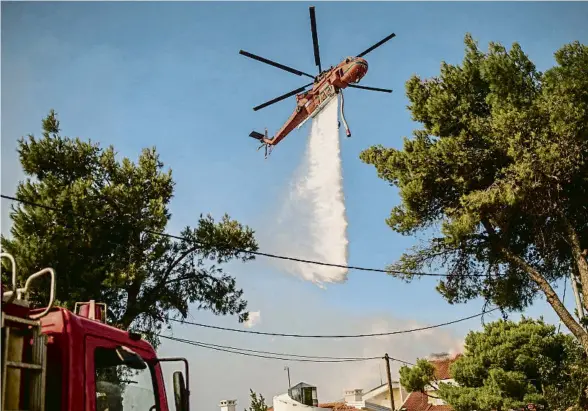  ?? ANGELOS TZORTZINIS / AFP ?? Un helicòpter llançant aigua ahir sobre les cases de Thrakomake­dones, a prop del mont Parnes, al nord d’Atenes