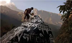  ??  ?? A Nepali Sherpa touches up the paint on a large Mani stone, which contains Buddhist prayers, near the village of Phakding, in Nepal. Photograph: Kevin Frayer/AP