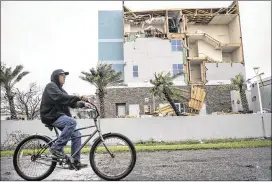  ?? TAMIR KALIFA / THE NEW YORK TIMES ?? Jeff Page rides his bike past a hotel damaged during Hurricane Harvey in Rockport, Texas, on Saturday. Rockport, a coastal city of about 10,000, was in the hurricane’s path when it came ashore late Friday.