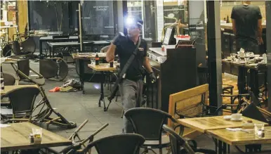  ?? (Flash90) ?? A POLICE OFFICER inspects the scene where two terrorists fired on a crowd of shoppers and diners last night at Tel Aviv’s Sarona Market, killing three and wounding seven.