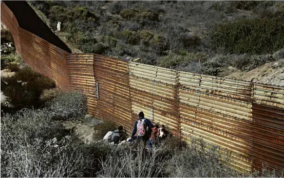  ?? Rebecca Blackwell/Associated Press ?? Com ajuda de “guias”, família de imigrantes tenta entrar nos EUA por buraco na fronteira do México, em Tijuana