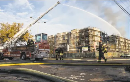  ?? Photos by Jessica Christian / The Chronicle ?? Fire crews pour water on a residentia­l complex under constructi­on in Oakland after a massive blaze tore through the site.