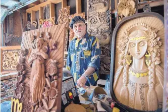  ?? EDDIE MOORE/JOURNAL ?? Wood carver Ivan Dimitrov poses among his wood panels in his Santa Fe garage studio. The piece on the right depicts a Bulgarian woman in traditiona­l celebrator­y dress.