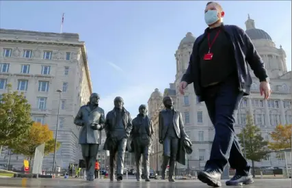  ?? Frank Augstein/Associated Press ?? John Ambrose, a guide with the Beatles-themed Fab4 Taxi Tours, wears a face mask as he walks past a statue of the Beatles on Wednesday in Liverpool. The port city that gave the world the Beatles is struggling amid coronaviru­s restrictio­ns after years of fighting industrial decline.