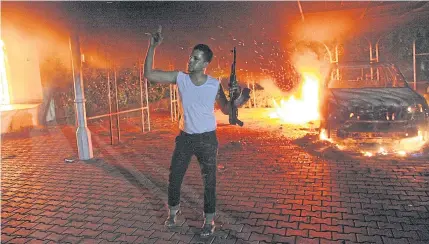  ?? AFP ?? A picture taken on Sept 11, 2012 shows an armed man waving his rifle as buildings and cars are engulfed in flames after being set on fire inside the US consulate compound in Benghazi.